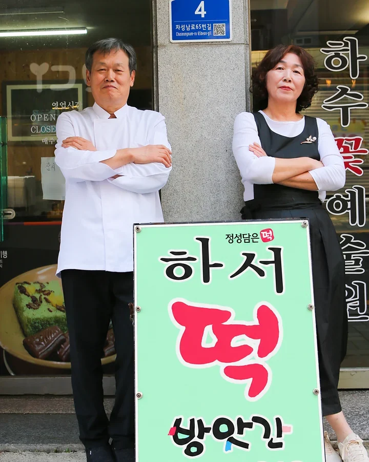 가게 앞 입간판 옆에 나란히 선 사장님 부부